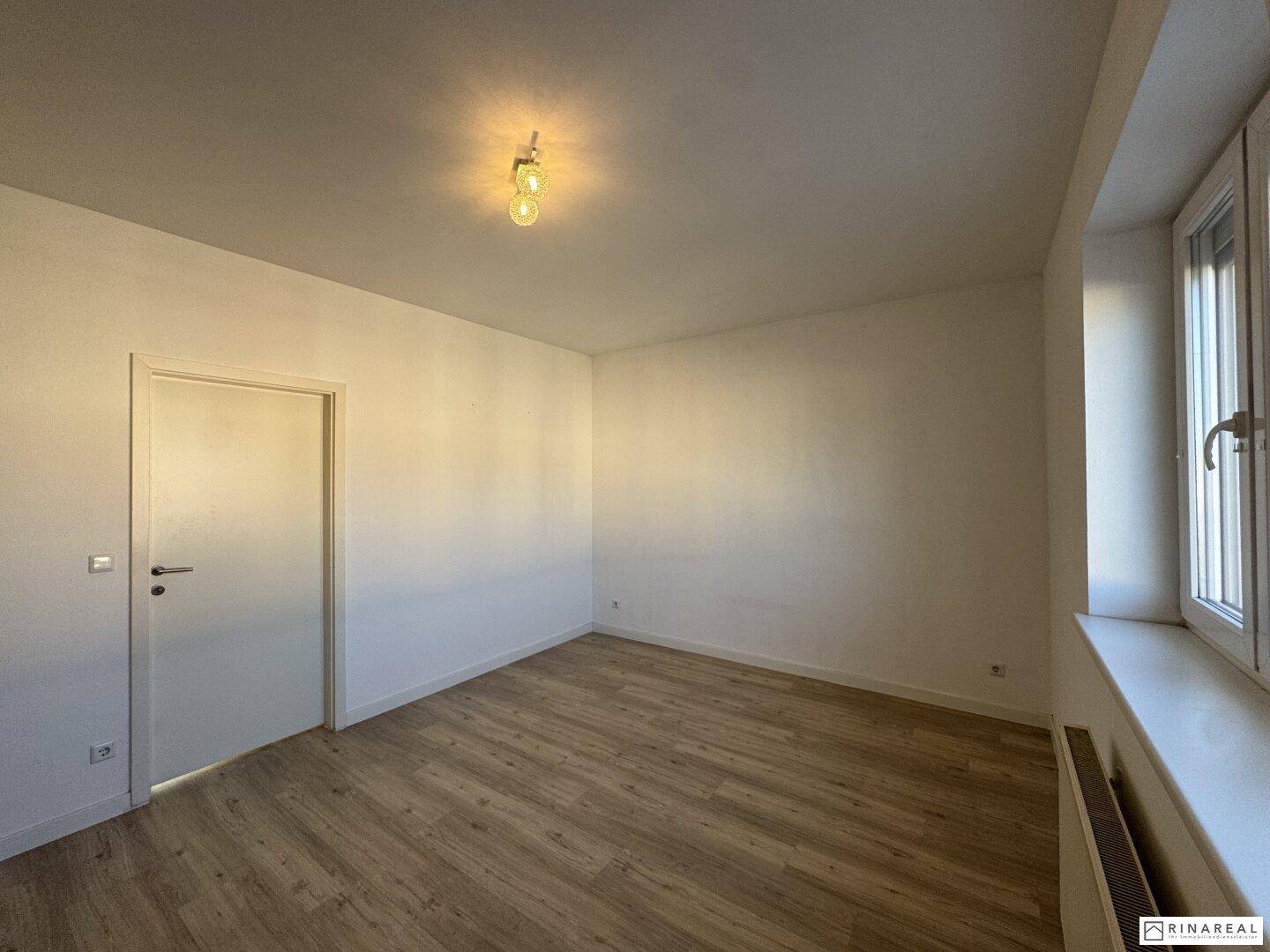 Helles Schlafzimmer mit Laminatboden und einem Fenster, das viel Tageslicht hereinlässt.