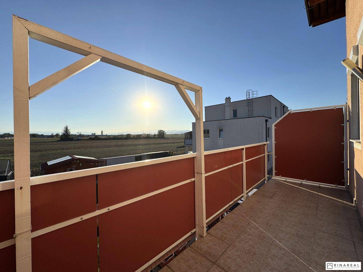 Sonniger Balkon mit braunen Sichtschutzelementen und weitem Blick über die Felder.