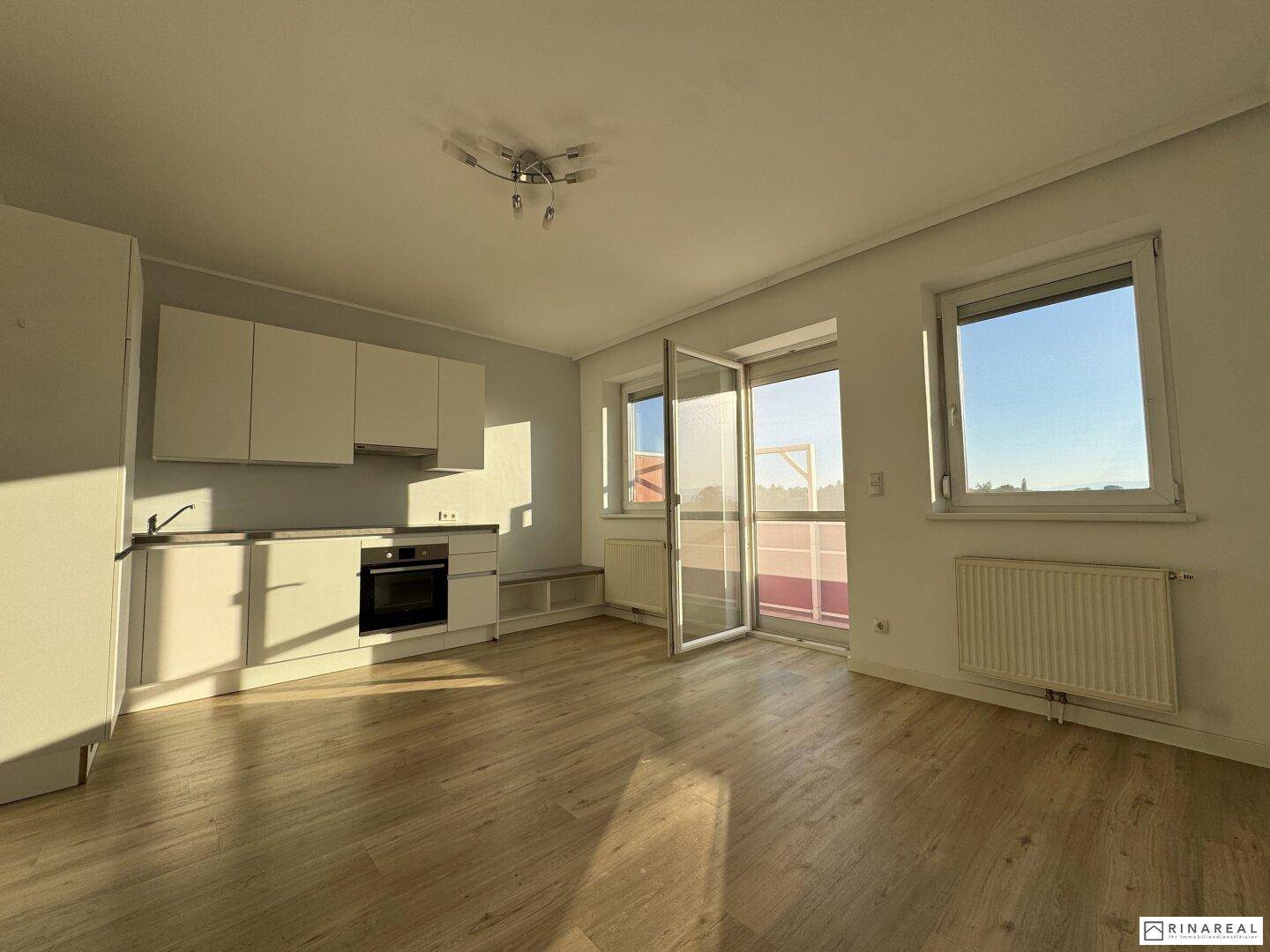 Lichtdurchfluteter Wohn- und Essbereich mit moderner Küchenzeile und Zugang zum sonnigen Balkon.