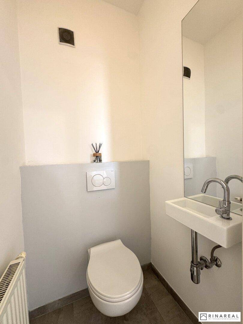Modernes Gäste-WC mit wandhängendem WC, kleinem Waschbecken und Lüftung.
