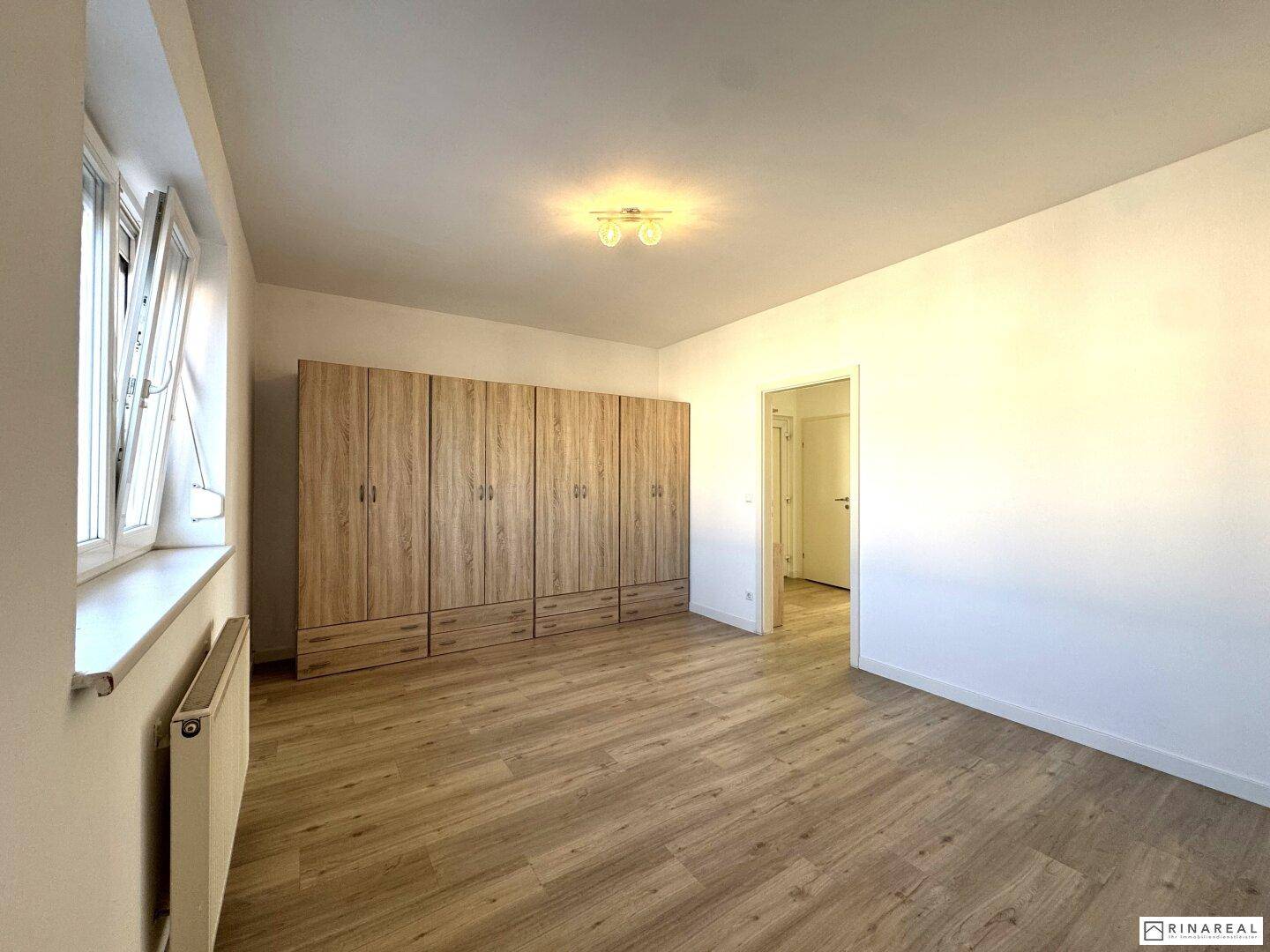 Geräumiges Schlafzimmer mit hellem Laminatboden und Platz für einen großen Kleiderschrank.