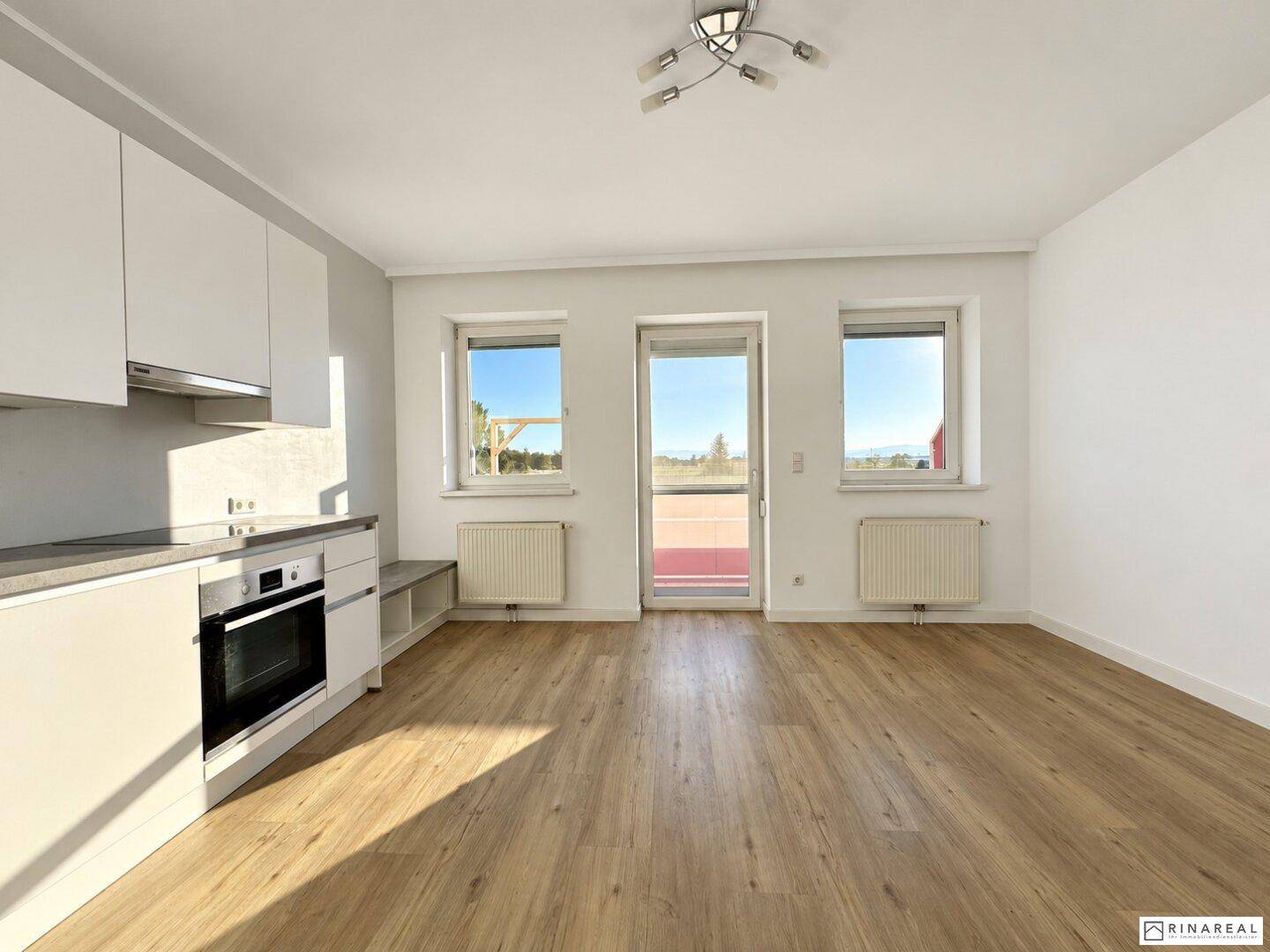 Offener Wohnbereich mit Küchenzeile, großen Fenstern und hellem Laminatboden, ideal für modernes Wohnen.