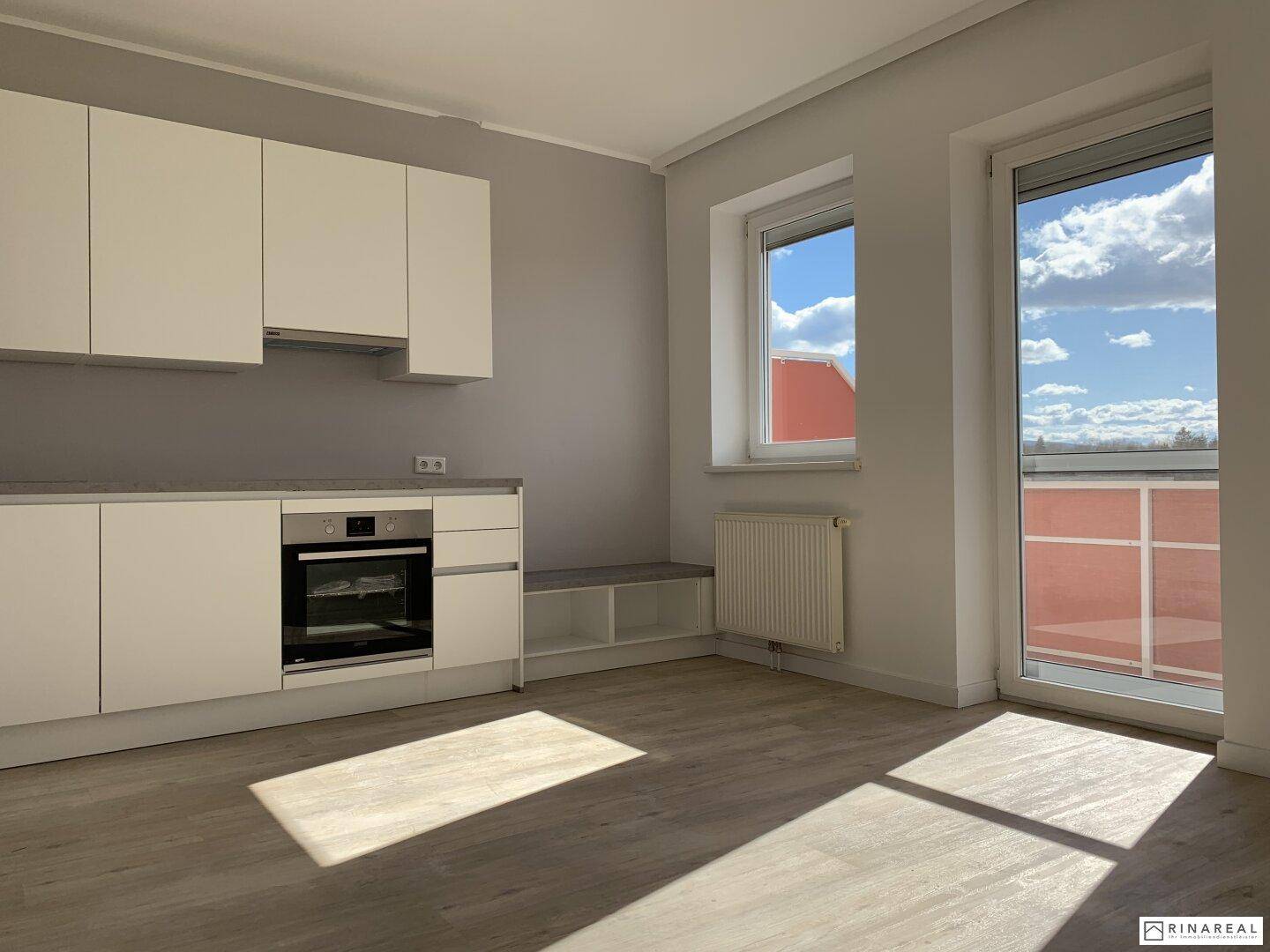 Heller Wohnbereich mit integrierter Küchenzeile, Laminatboden und Zugang zum Balkon.