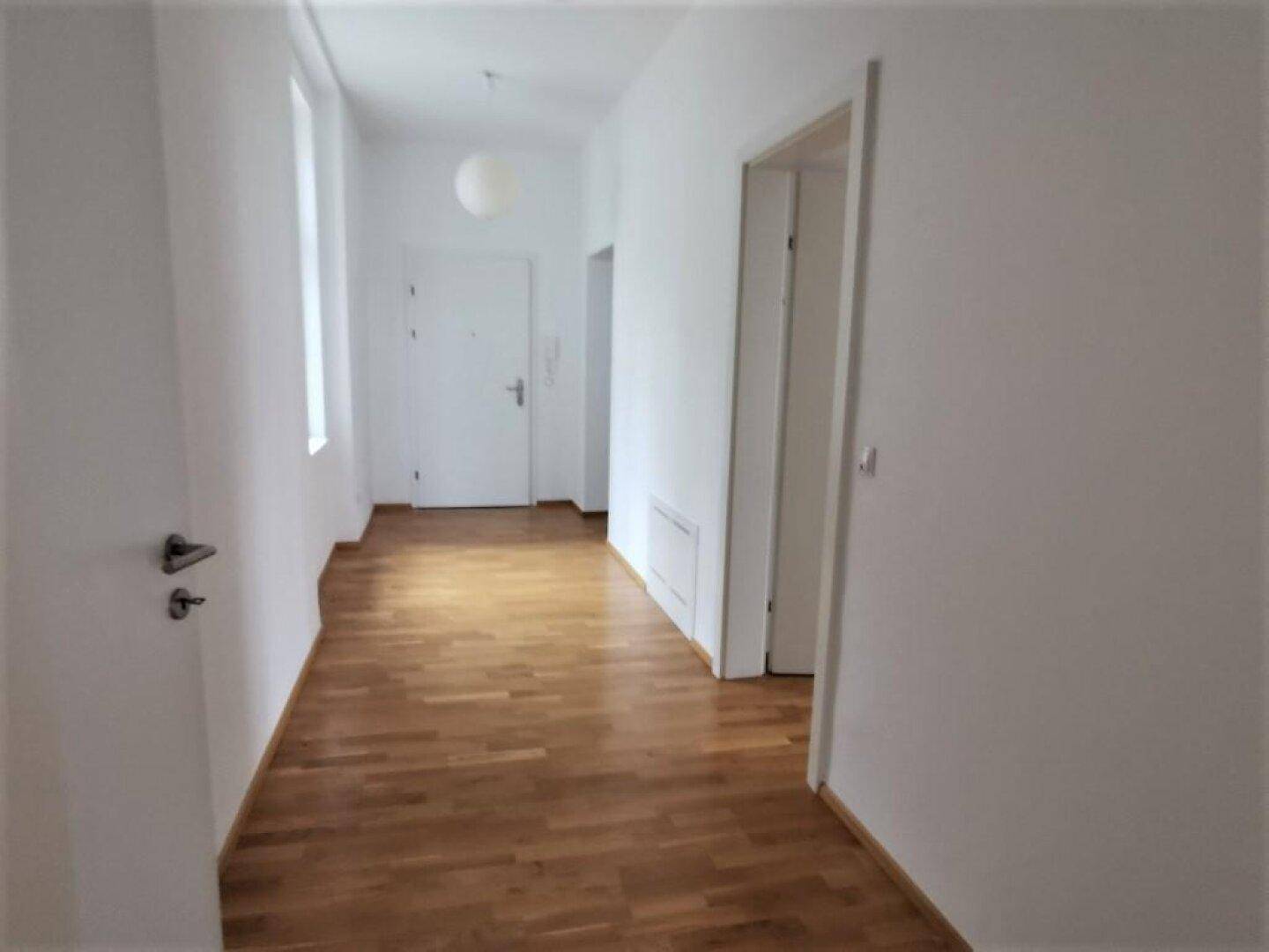 Heller Flur mit Holzboden und weiß gestrichenen Wänden, der zu weiteren Räumen führt.