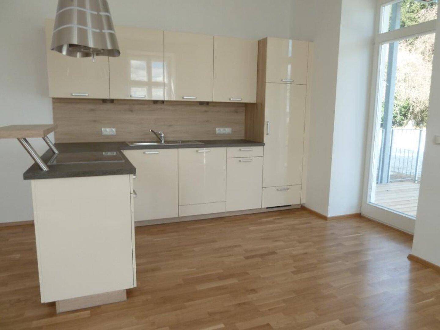 Helle Einbauküche in Beige mit glänzenden Fronten und direktem Zugang zum Balkon.
