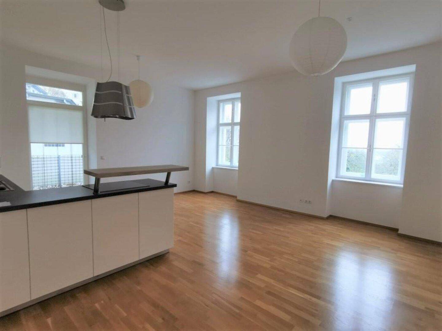 Geräumiger Wohn-Essbereich mit Holzboden, großen Fenstern und moderner Beleuchtung.