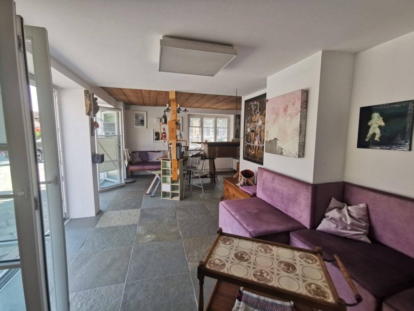 Gemütlicher Wohnbereich mit Steinboden, lila Sofas und rustikalen Holzbalken an der Decke.
