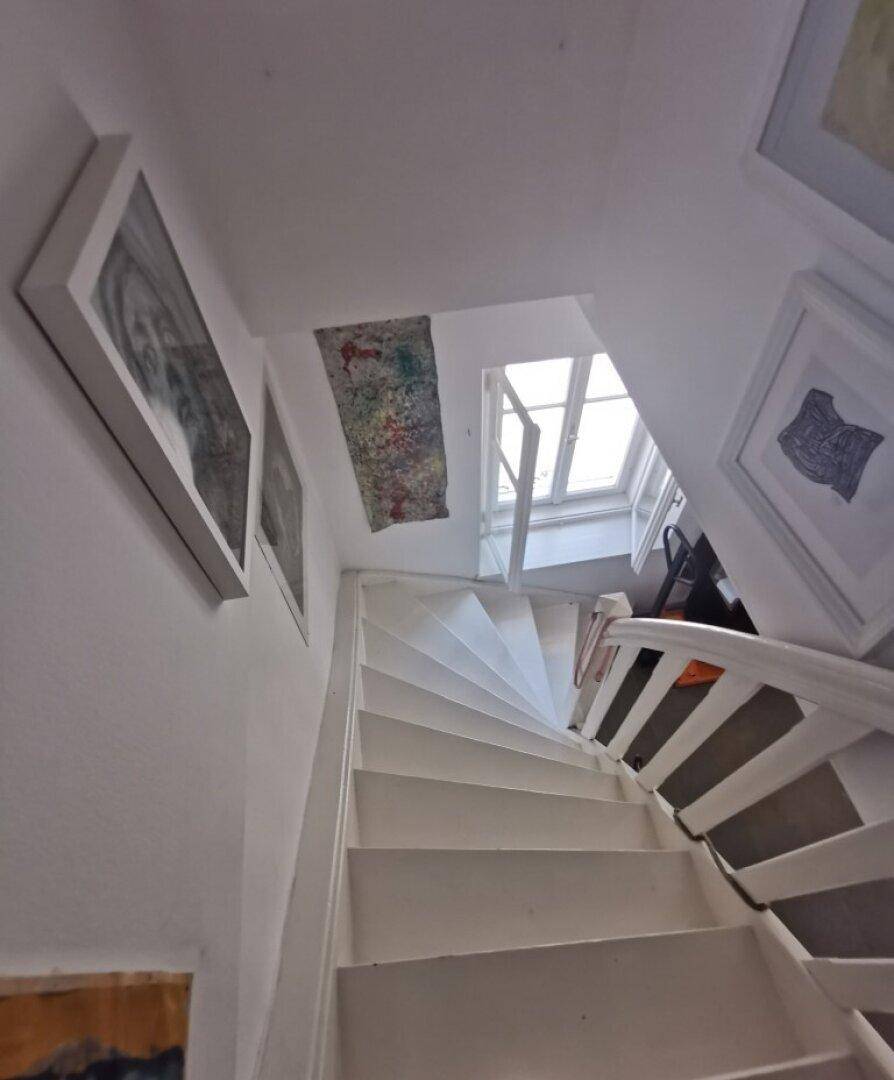 Helles Treppenhaus mit weiß gestrichenen Stufen und einem Oberlicht für natürliches Licht.