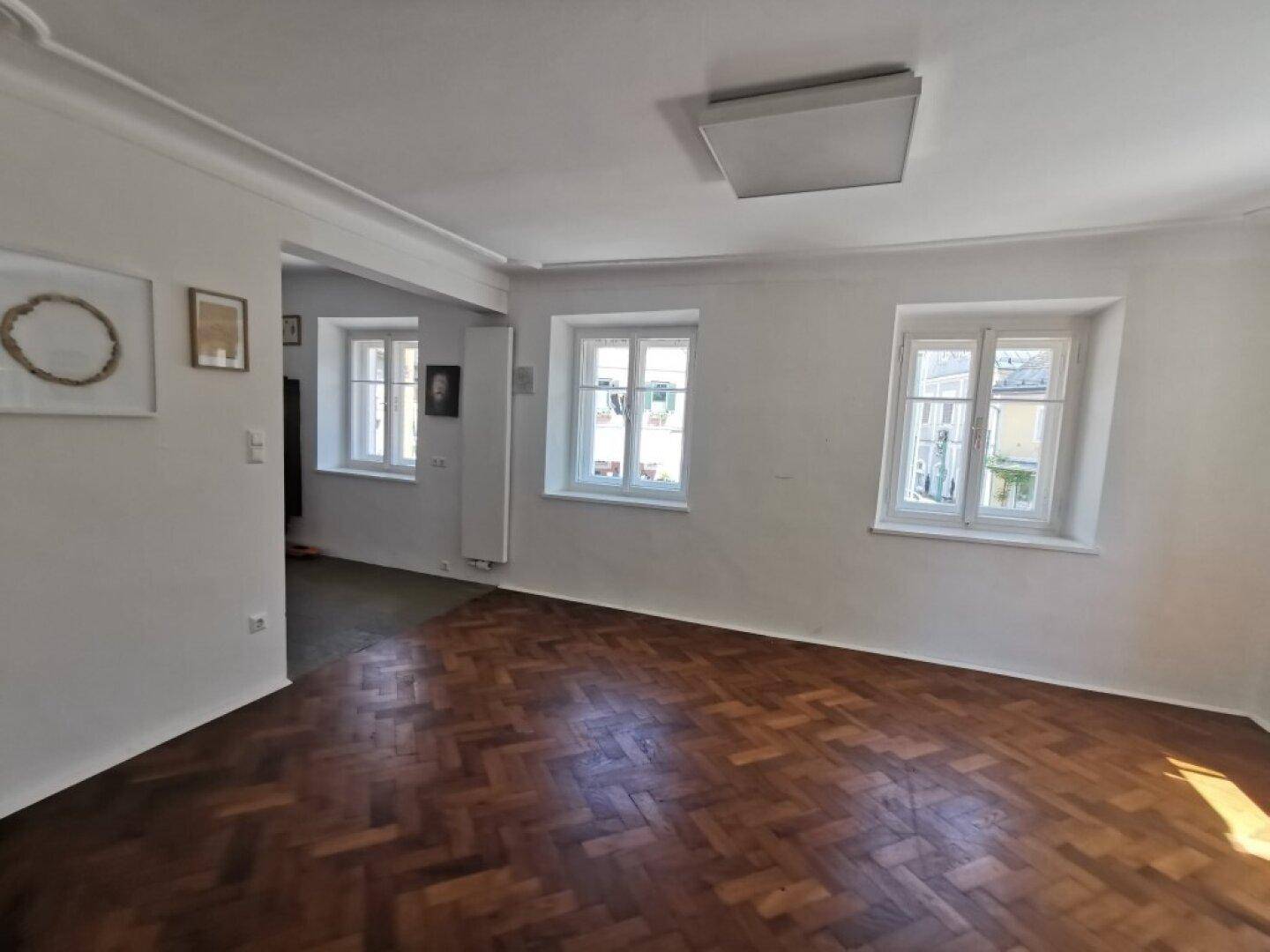 Lichtdurchfluteter Wohnbereich mit Fischgrätparkett und mehreren Fenstern, die den Raum erhellen.