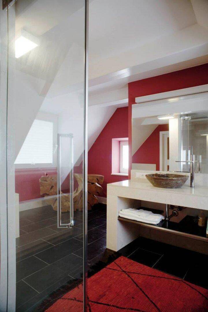 Modernes Badezimmer mit roter Akzentwand, Glasdusche und stilvollem Aufsatzwaschbecken.