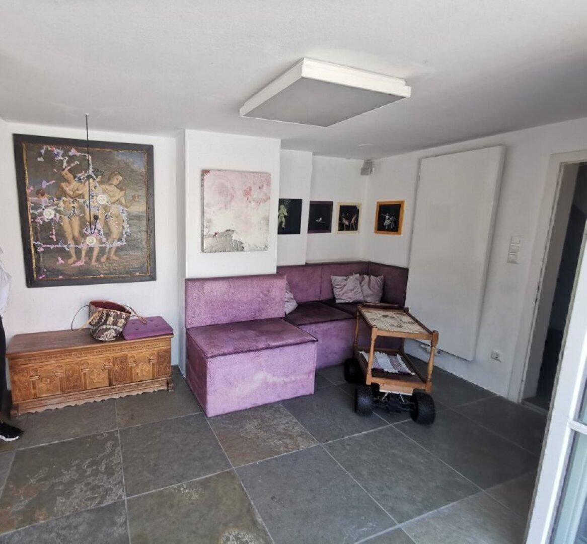 Gemütlicher Wohnbereich mit Steinboden, lila Sofas und Kunstwerken an den Wänden.