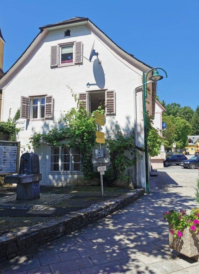 Seitenansicht eines historischen Gebäudes mit grüner Bepflanzung und traditionellen Fensterläden.
