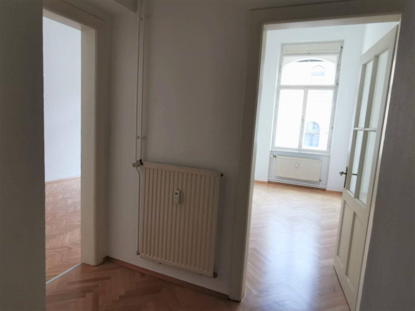 Flur mit Heizkörper und Blick in angrenzende Zimmer mit Parkettboden und Fenstern.