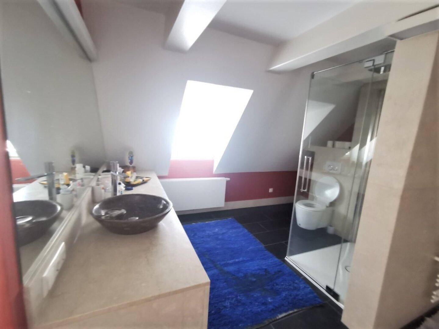 Modernes Badezimmer mit Waschtisch, Spiegel und Glasdusche unter einem Dachfenster.