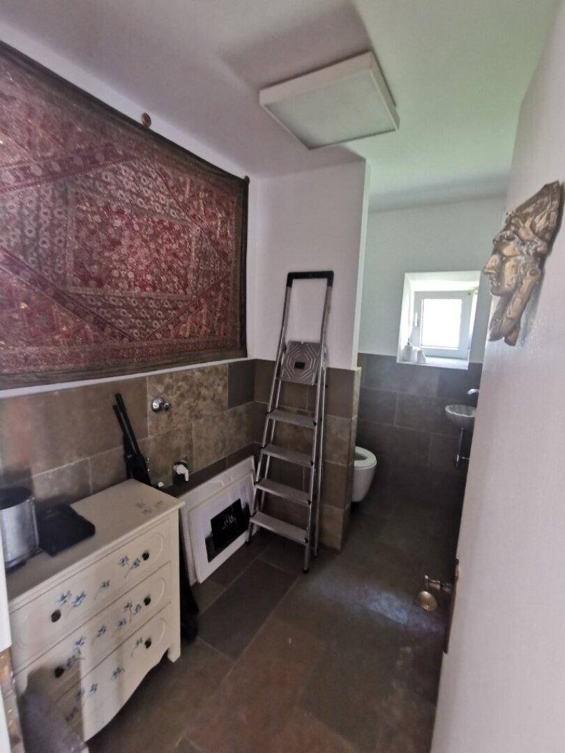 Kleines WC mit Steinboden, Wandteppich und einem Fenster für natürliche Belüftung.