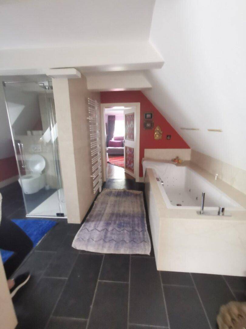 Großes Badezimmer mit Badewanne, Glasdusche und Zugang zu einem weiteren Raum.