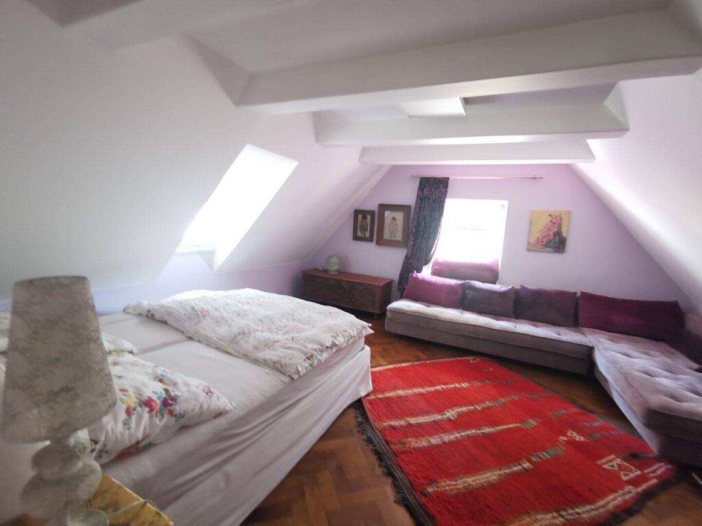 Gemütliches Schlafzimmer im Dachgeschoss mit Holzboden, Bett und Sofa unter schrägen Wänden.