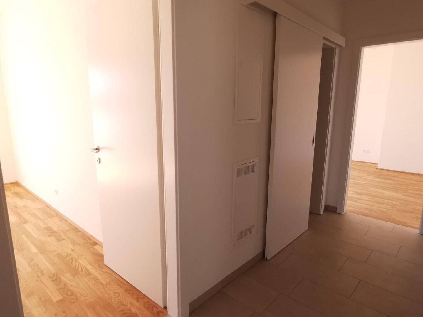 Heller Flur mit Fliesenboden und Schiebetüren, der zu den angrenzenden Zimmern führt.