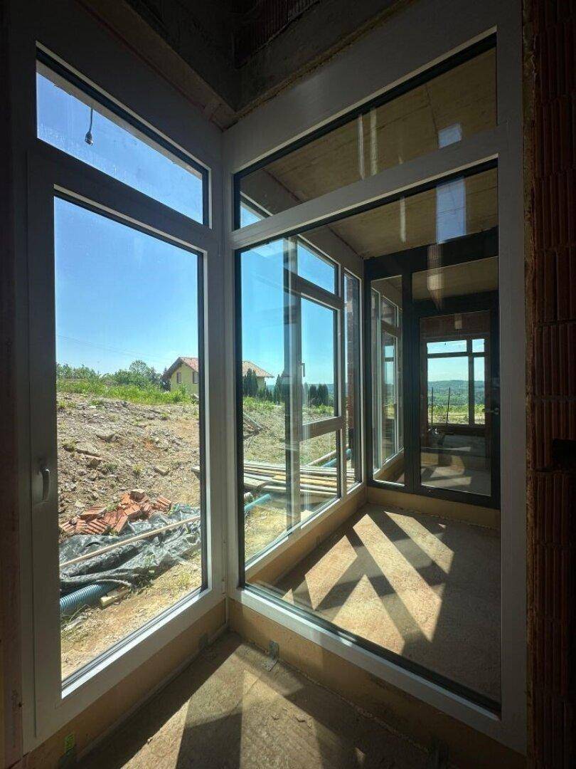Heller Innenraum im Rohbau mit großen Eckfenstern und weitem Ausblick.