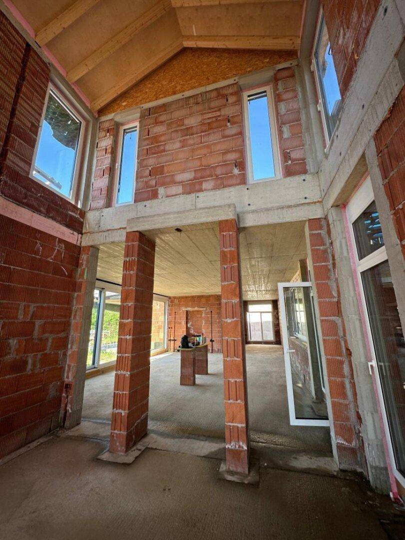 Geräumiger Rohbau mit hohen Decken, Ziegelwänden und Betonstützen.