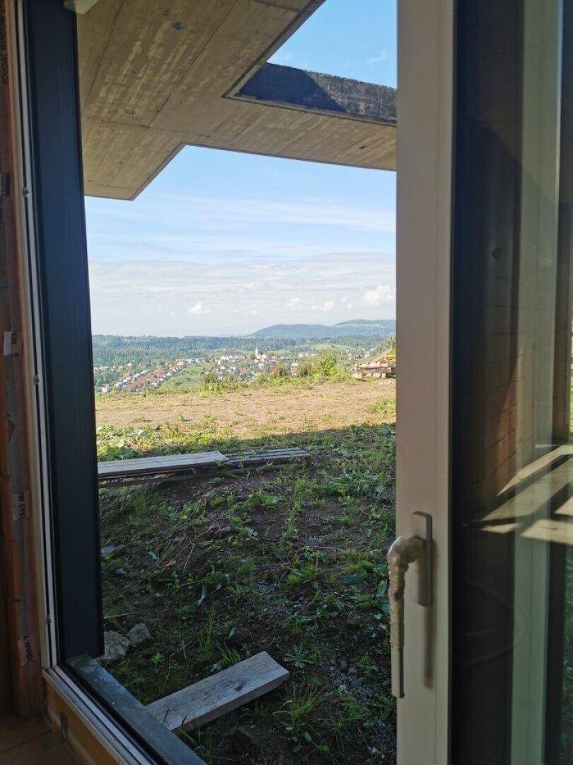 Blick aus einem Fenster im Rohbau auf die weite Landschaft und eine Siedlung.