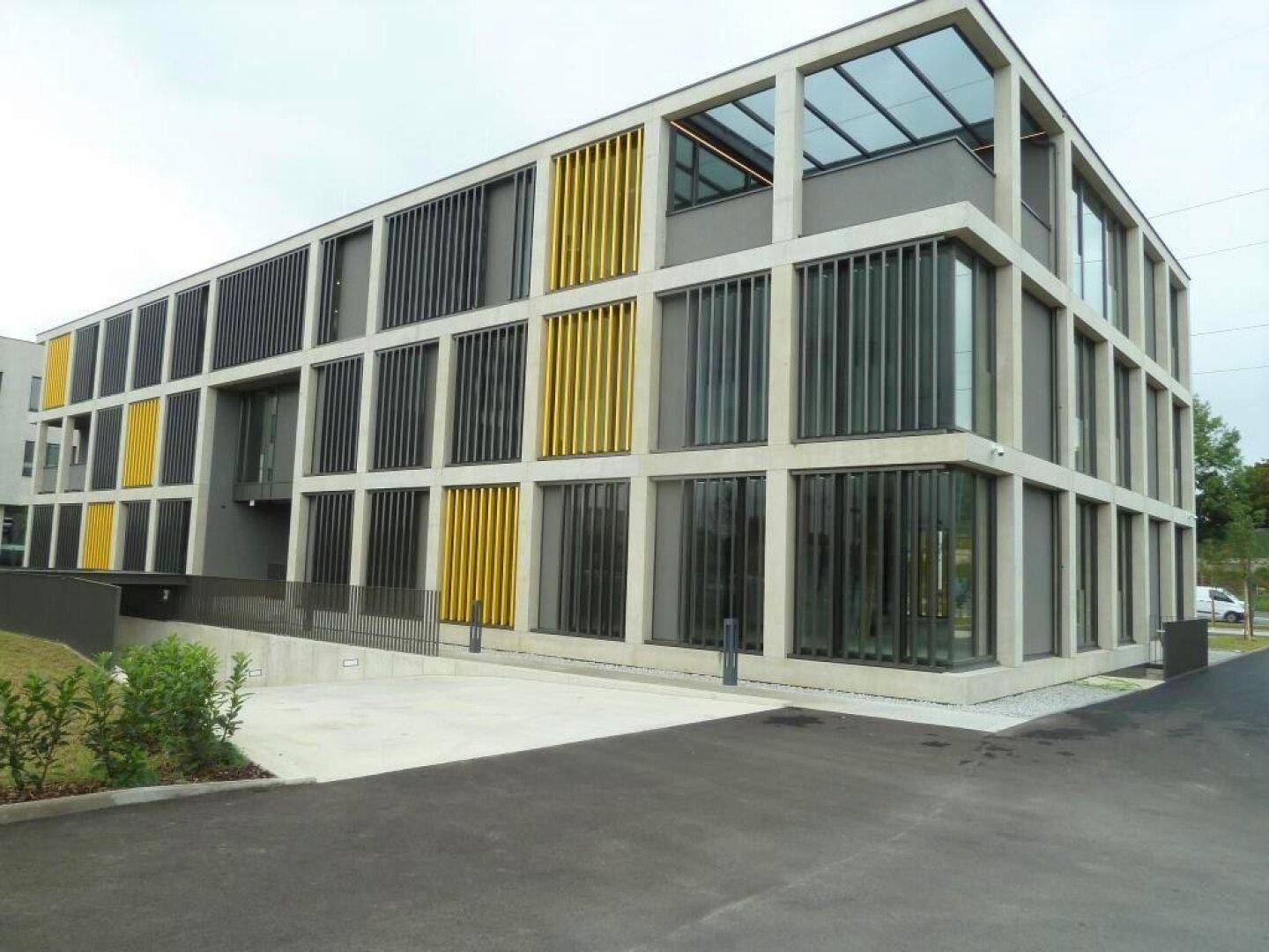 Modernes Bürogebäude mit markanter Architektur, gelben Akzenten und einer Zufahrt zum Untergeschoss.