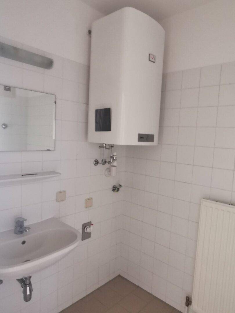 Badezimmer mit Waschbecken, Wandfliesen und einem großen Warmwasserboiler an der Wand.