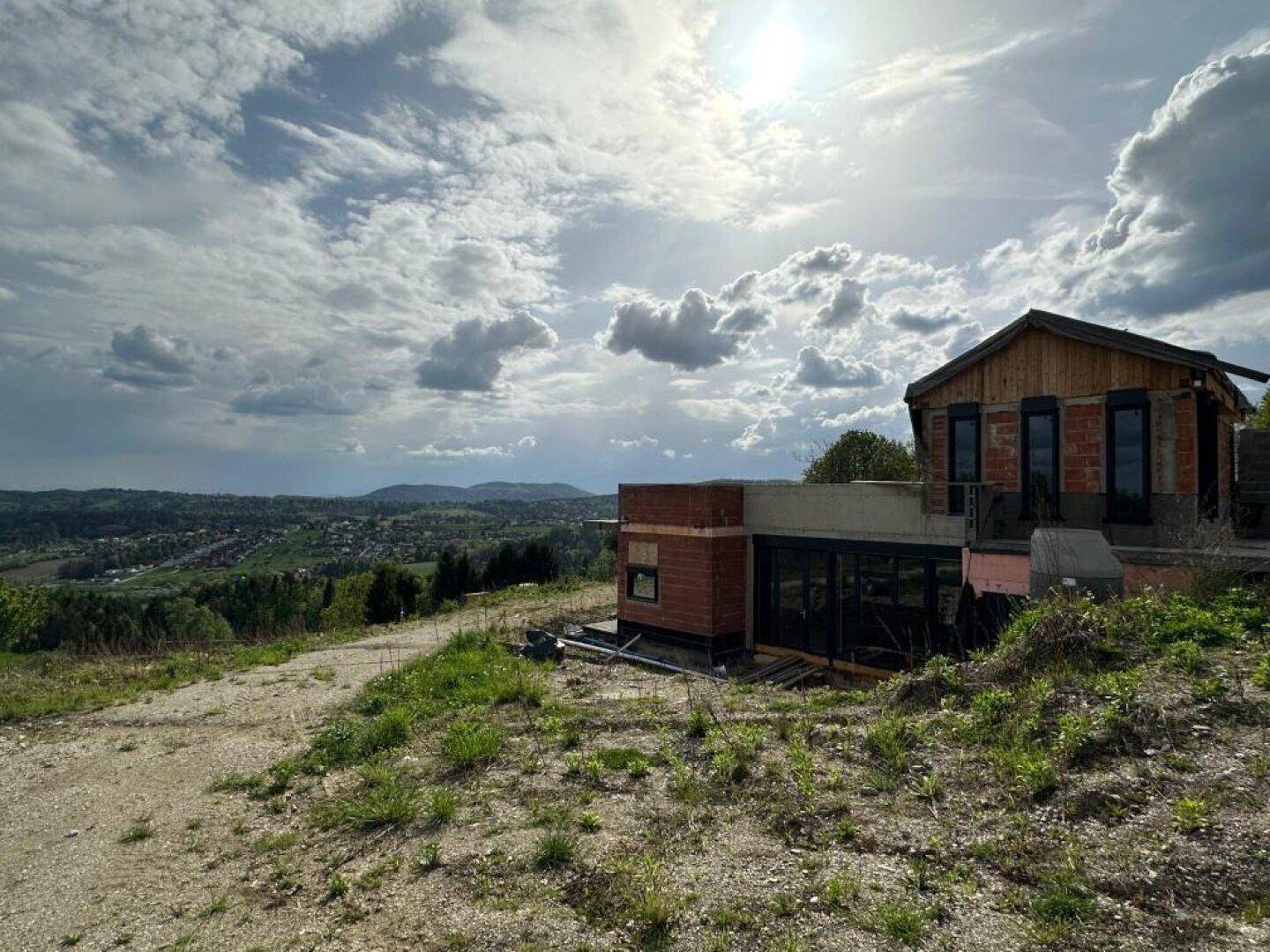 Neubau in Hanglage mit weitem Ausblick über die grüne Landschaft unter bewölktem Himmel.