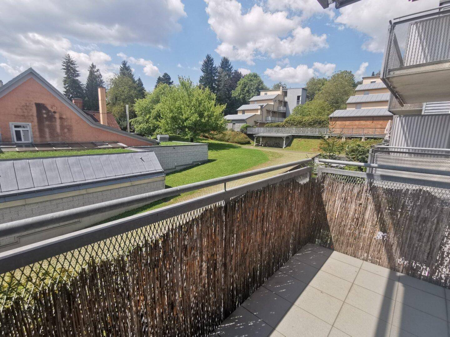 Balkon mit Holzsichtschutz und Blick auf die grüne Umgebung und weitere Gebäude.