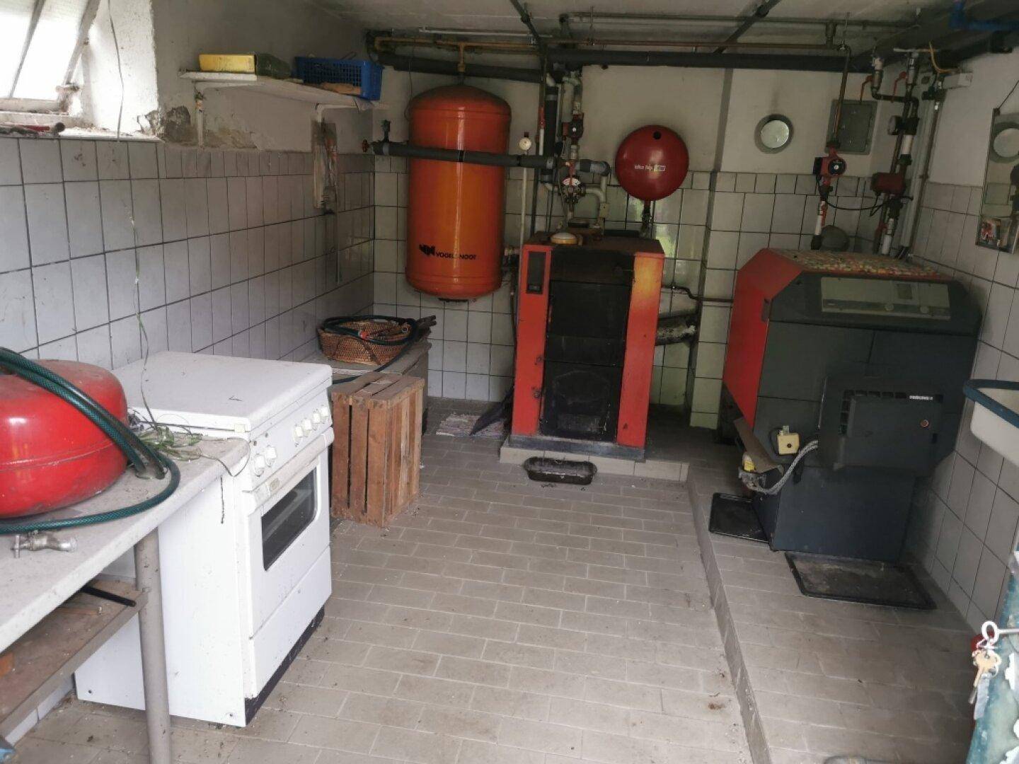 Heizungsraum mit zwei Heizkesseln, Warmwasserspeicher und gefliesten Wänden und Boden.