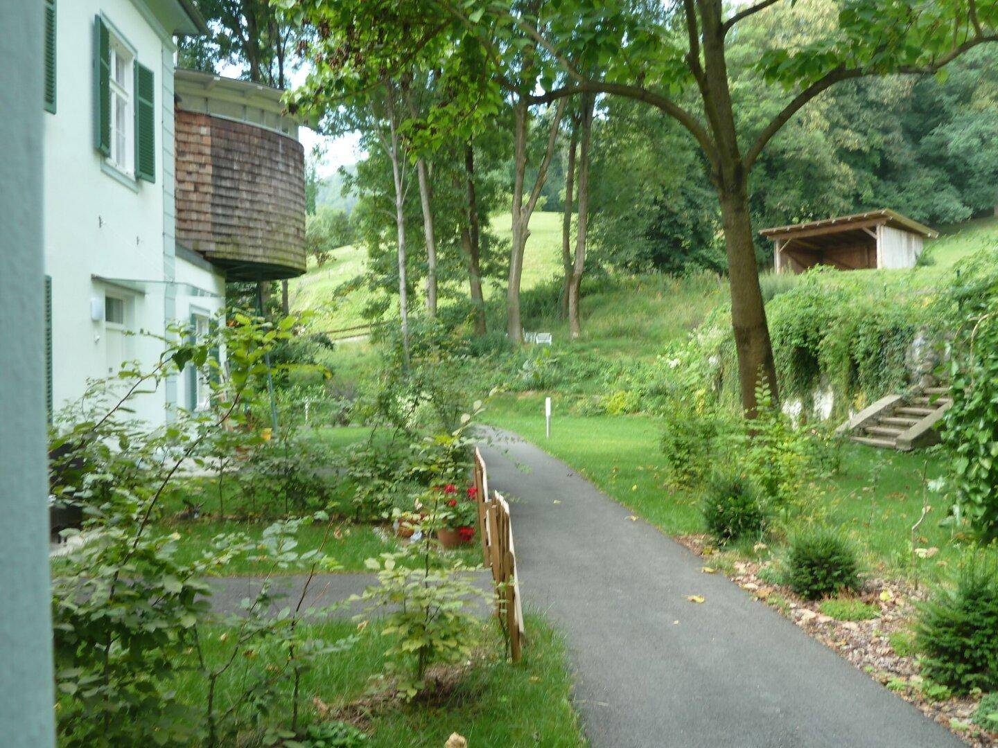 Gepflegter Gartenweg entlang des Hauses mit üppiger Vegetation und Blick auf die Hügellandschaft.
