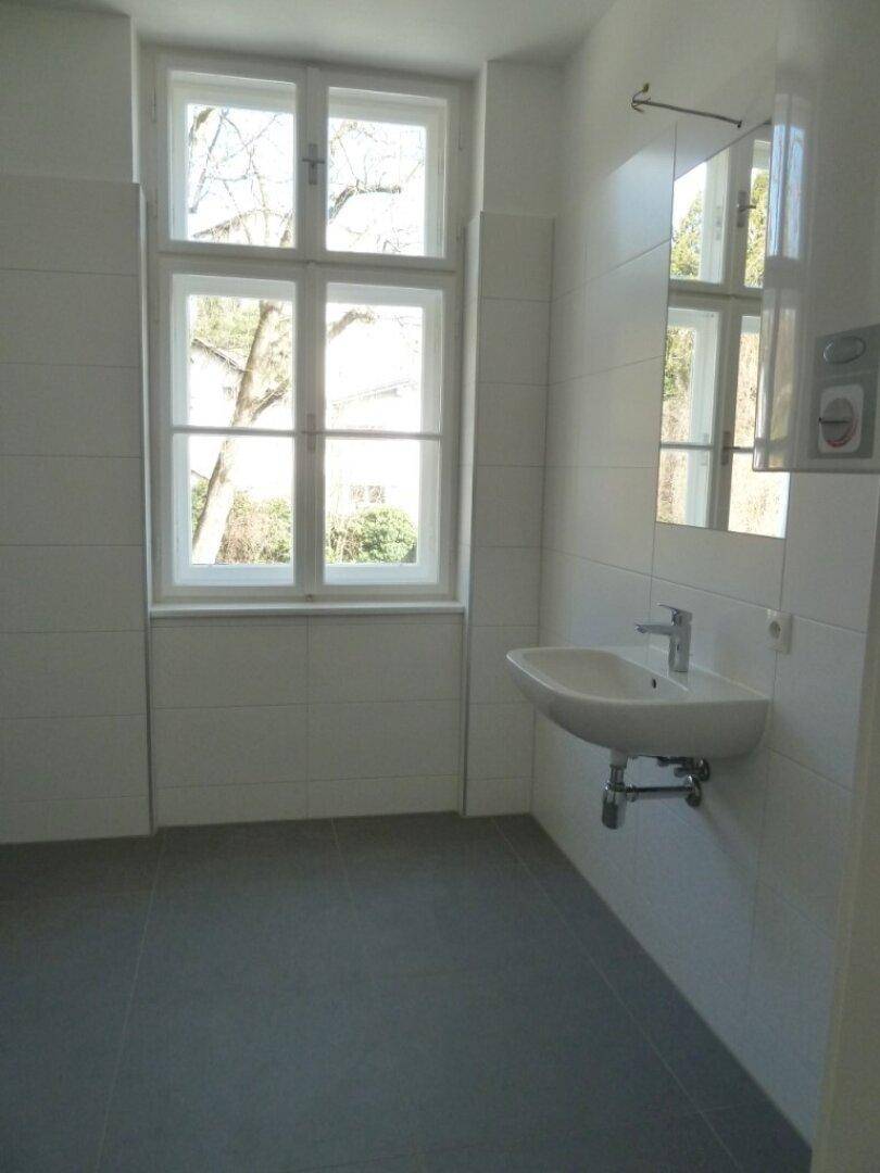 Helles Badezimmer mit Fenster, weiß gefliesten Wänden und modernem Waschbecken.