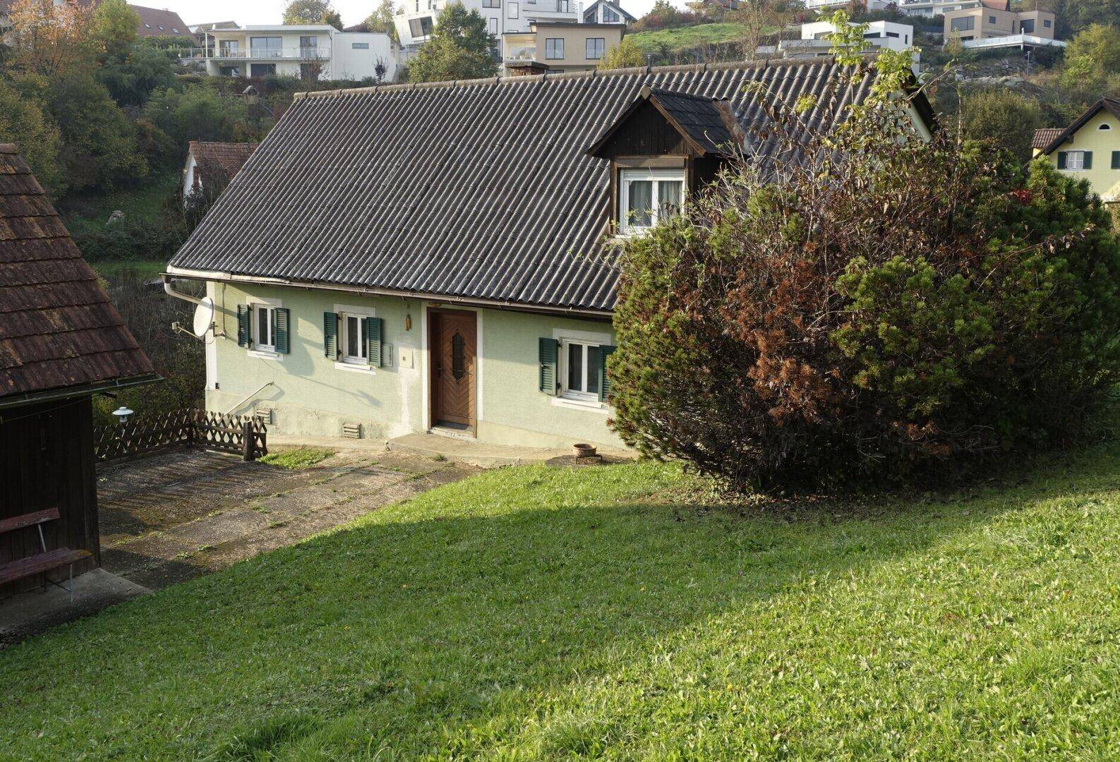 Vorderansicht des Hauses mit grünem Rasen, Büschen und einer Auffahrt unter bewölktem Himmel.