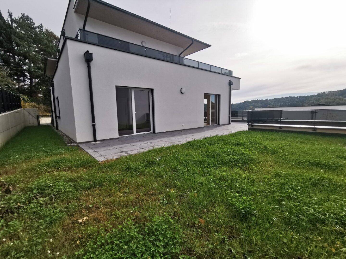 Modernes Wohngebäude mit weißer Fassade, Terrasse und gepflegter Rasenfläche.