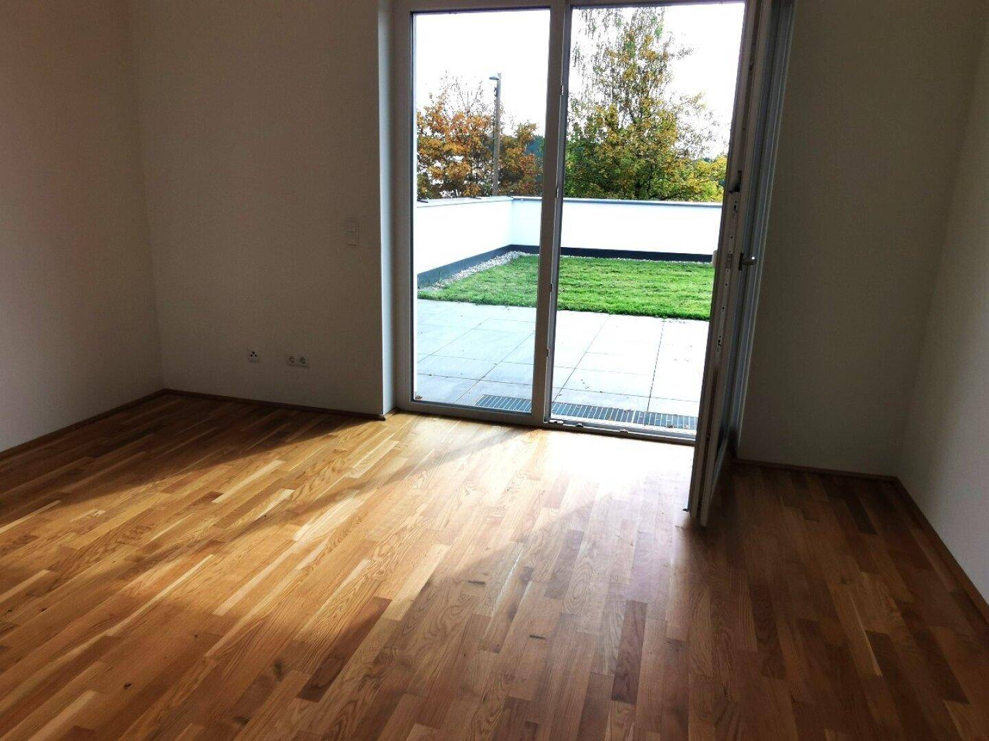 Schlafzimmer mit Holzboden und Zugang zu einer kleinen Terrasse mit Rasenfläche.