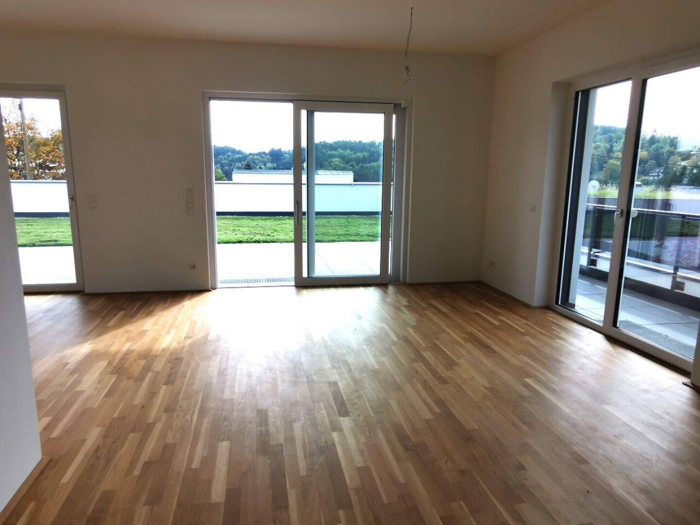 Geräumiges Wohnzimmer mit hellem Holzboden und Zugang zu einer großen Außenterrasse.