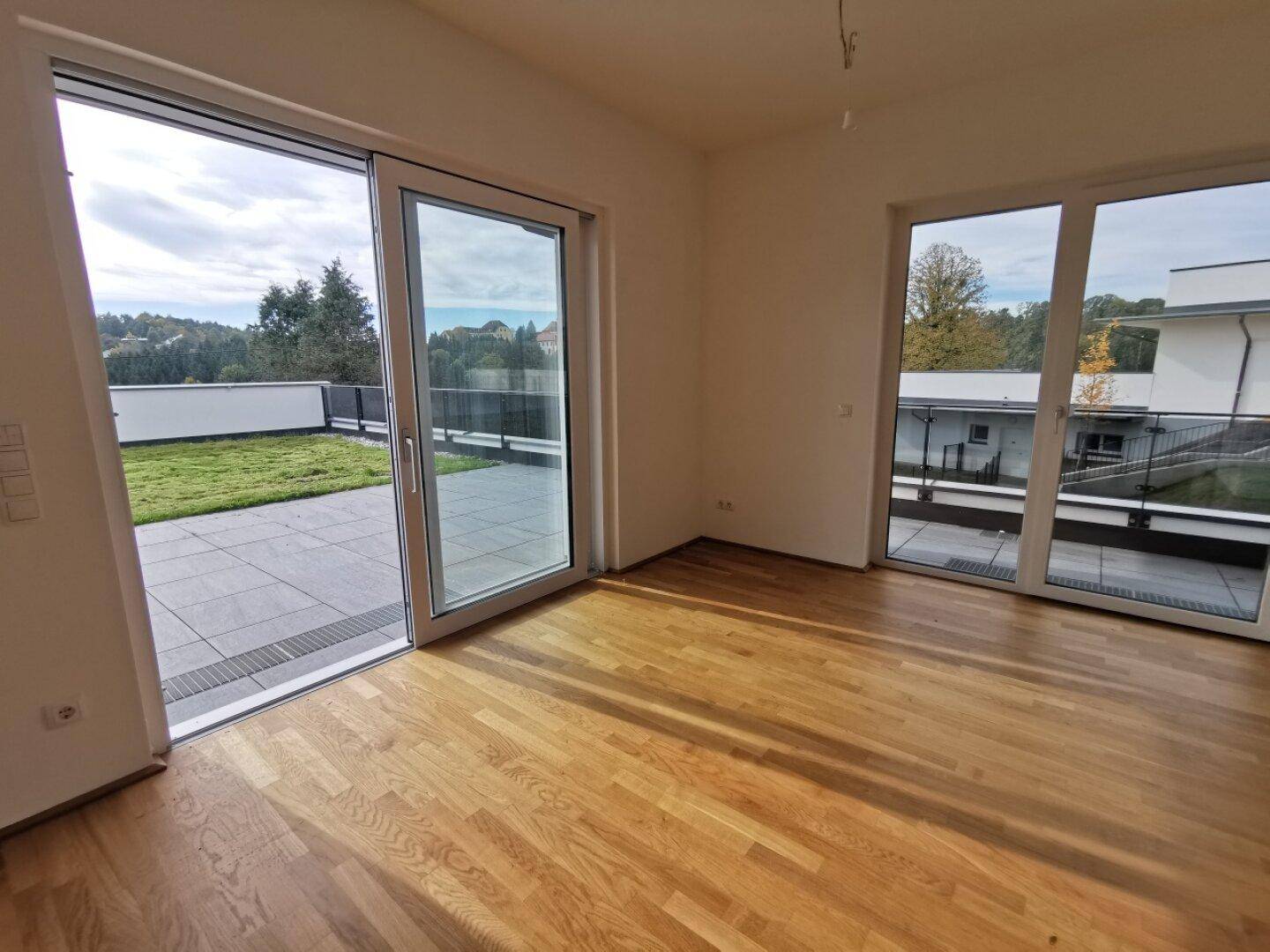 Helles Wohnzimmer mit Holzboden und großen Schiebetüren, die auf eine Terrasse führen.