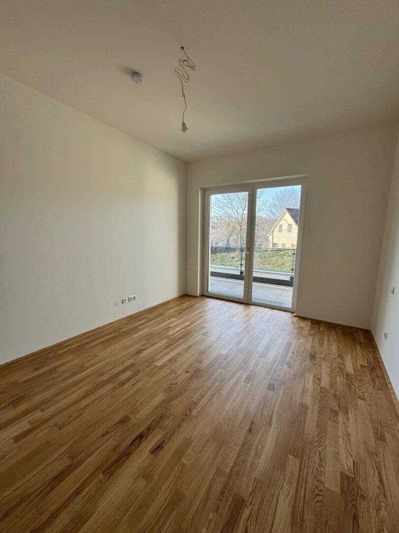 Geräumiges Schlafzimmer mit hellem Holzboden und Zugang zu einem kleinen Balkon oder einer Terrasse.