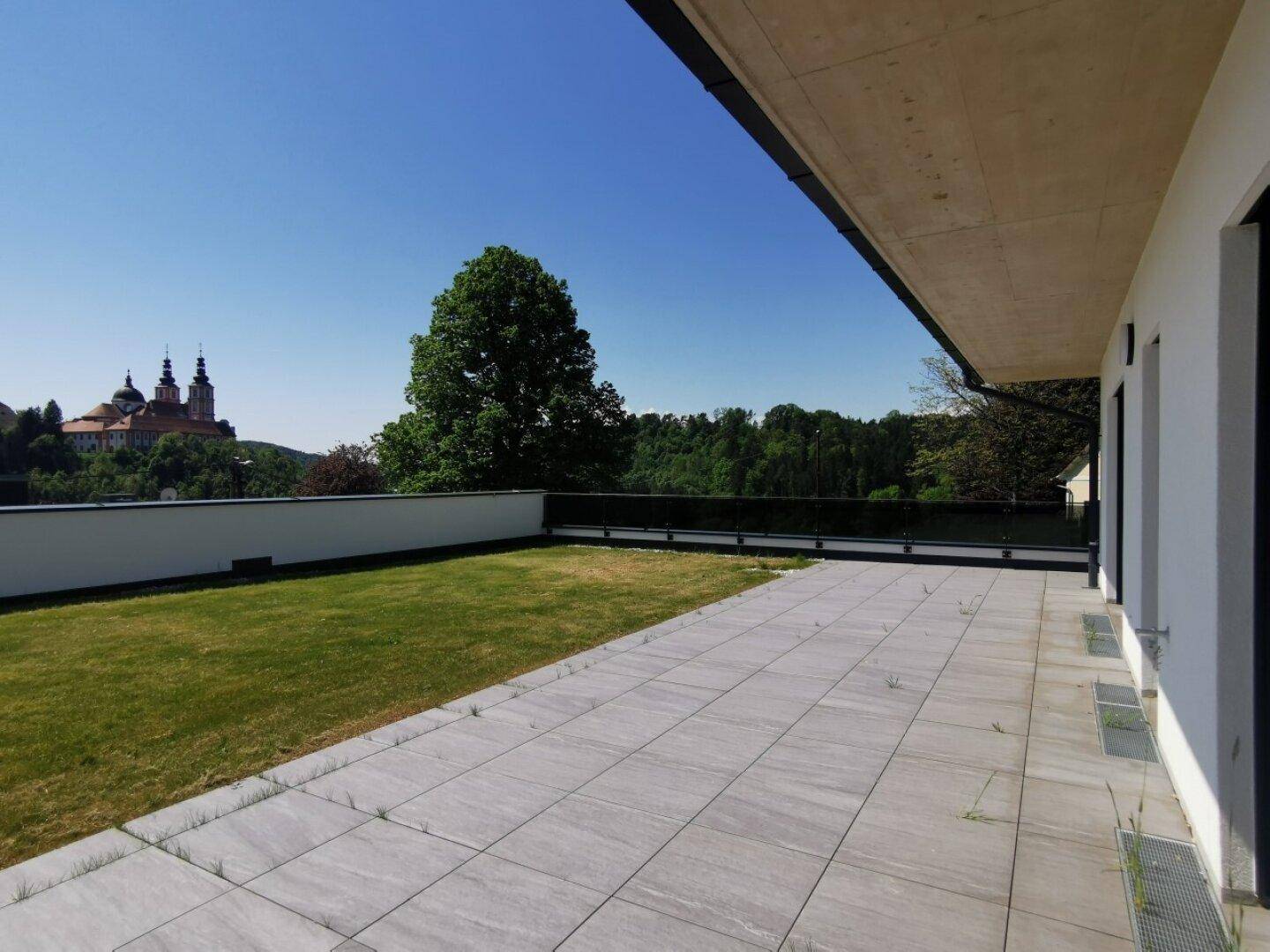 Weitläufige Terrasse mit Rasen und Blick auf die umliegende Landschaft und ein historisches Gebäude.