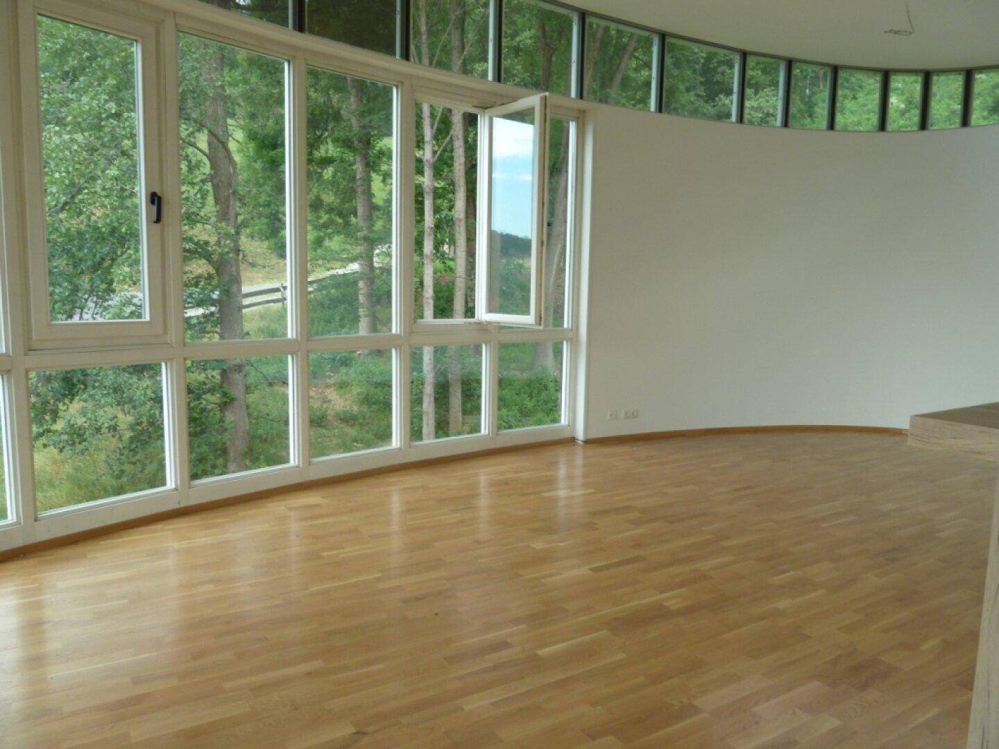 Lichtdurchfluteter Wohnraum mit geschwungenen Panoramafenstern und weitem Blick ins Grüne.