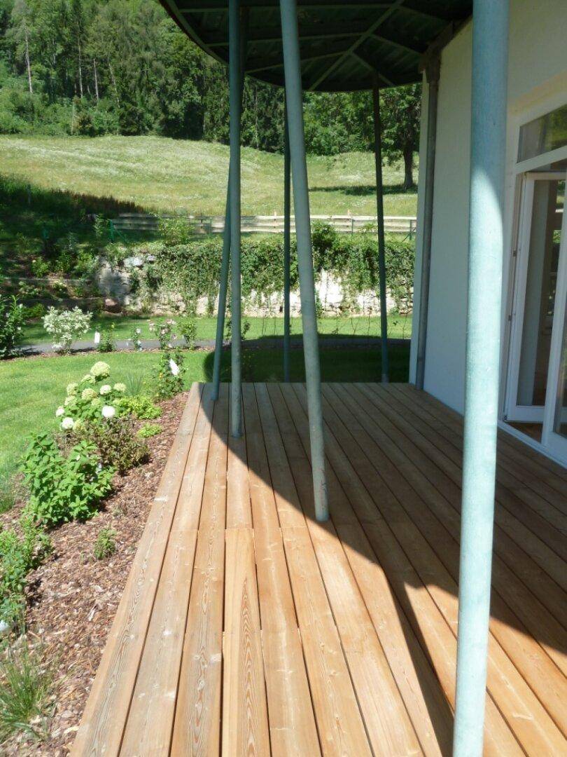 Holzterrasse mit Säulen und Blick auf den gepflegten Garten und die umliegende Natur.