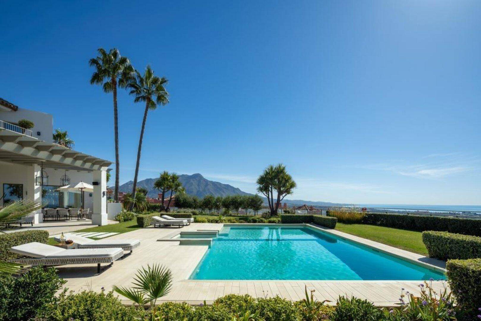 Weitläufiger Garten mit Pool, Liegeflächen und Panoramablick auf Meer und Berge.