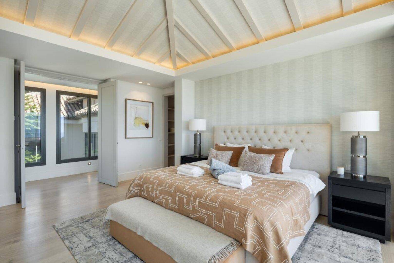 Helles Schlafzimmer mit hoher Decke, großem Bett und Zugang zu weiteren Räumen.