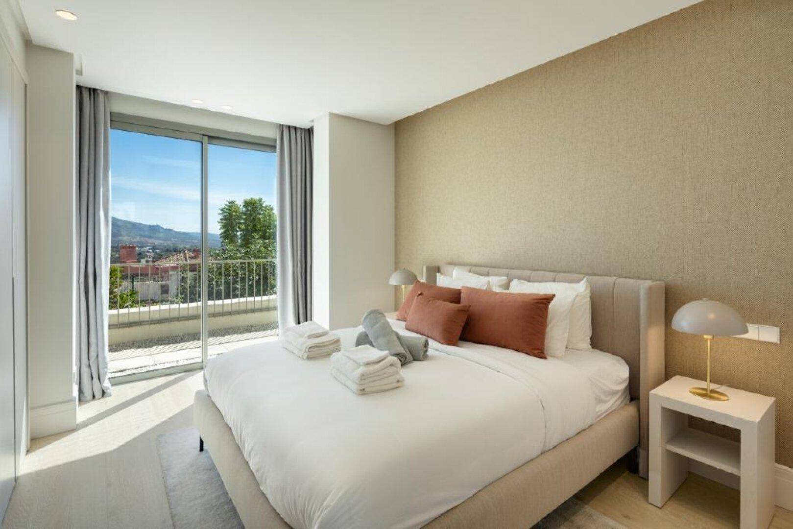 Helles Schlafzimmer mit Balkonzugang und Blick auf die grüne Umgebung.