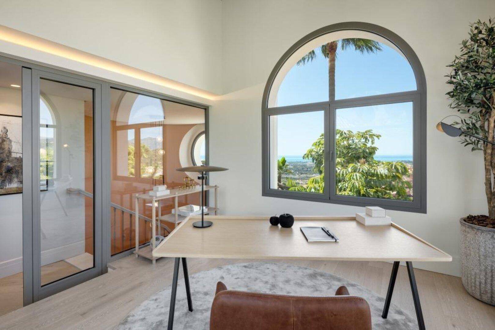 Helles Büro mit großem Bogenfenster, das einen weiten Blick auf die Landschaft und das Meer bietet.