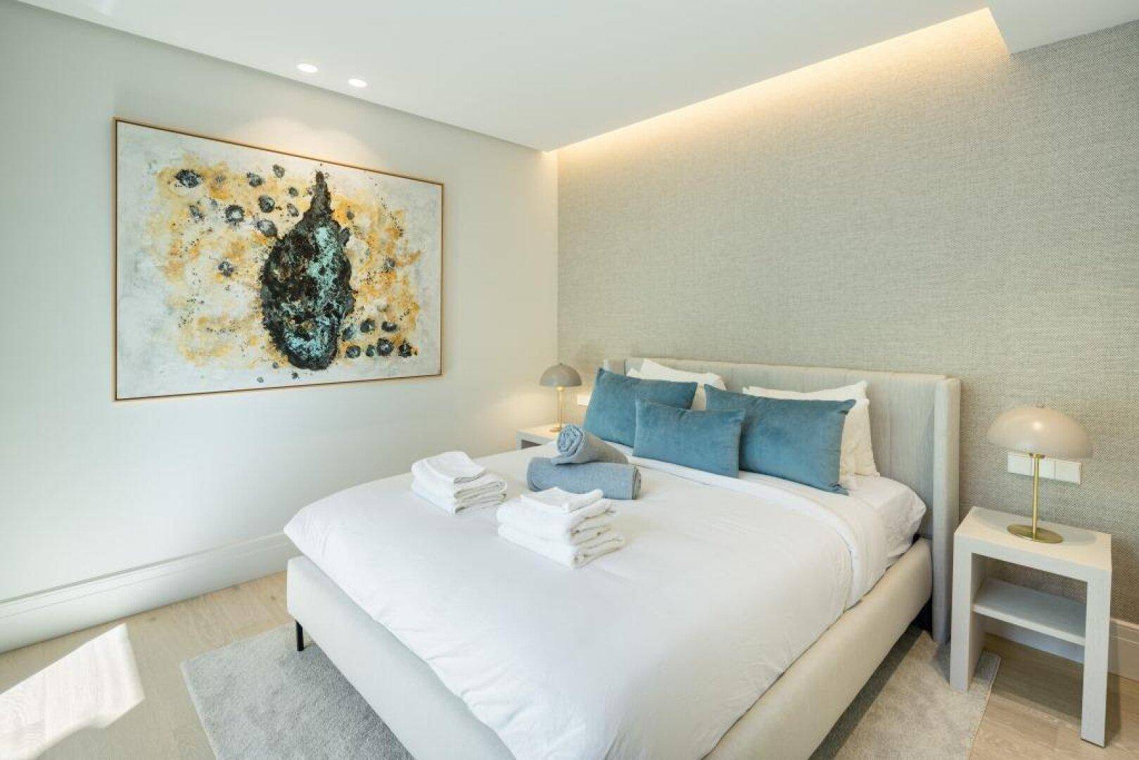 Gemütliches Schlafzimmer mit großem Bett, moderner Kunst an der Wand und indirekter Beleuchtung.