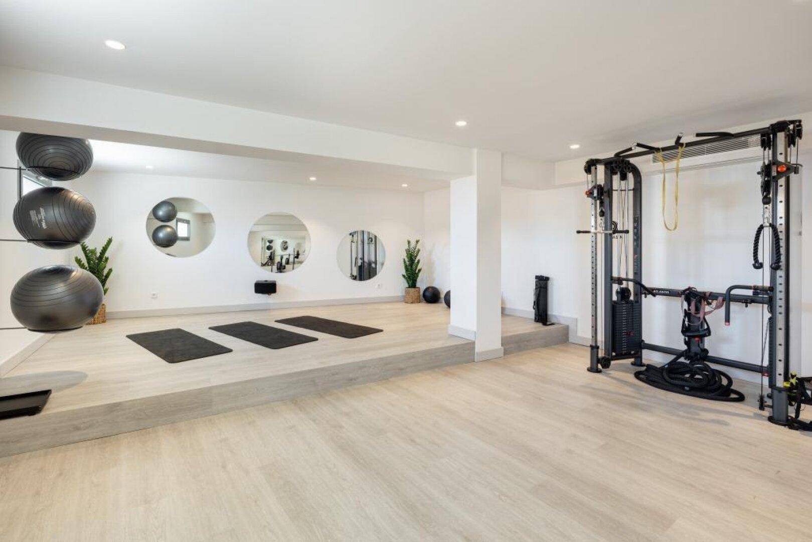 Geräumiger Fitnessraum mit verschiedenen Trainingsgeräten und einer erhöhten Fläche für Yoga.