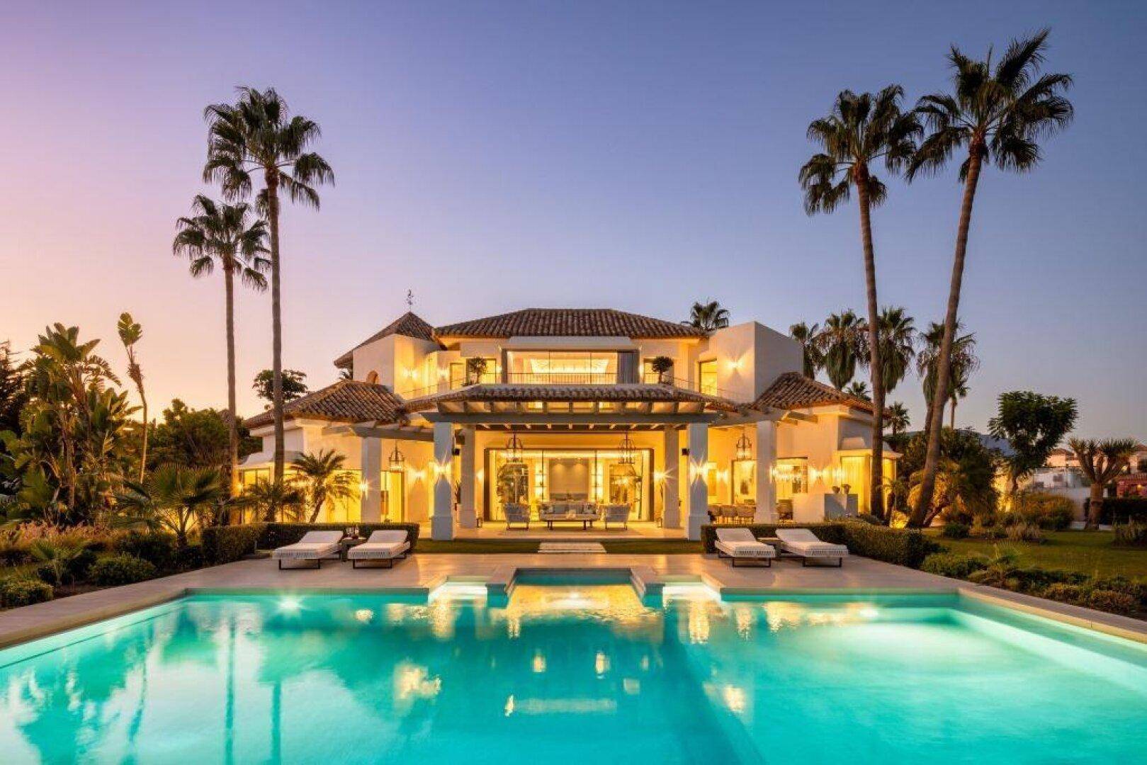 Luxuriöse Villa mit großem Poolbereich und Palmen bei Sonnenuntergang.