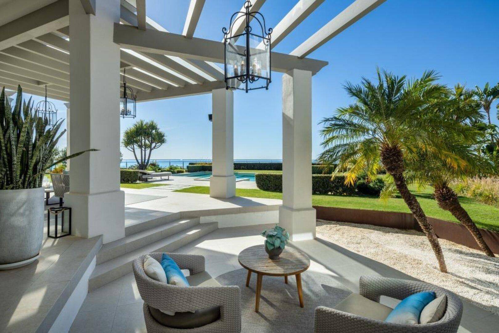 Überdachte Terrasse mit bequemen Sitzgelegenheiten und herrlichem Blick auf Pool und Meer.