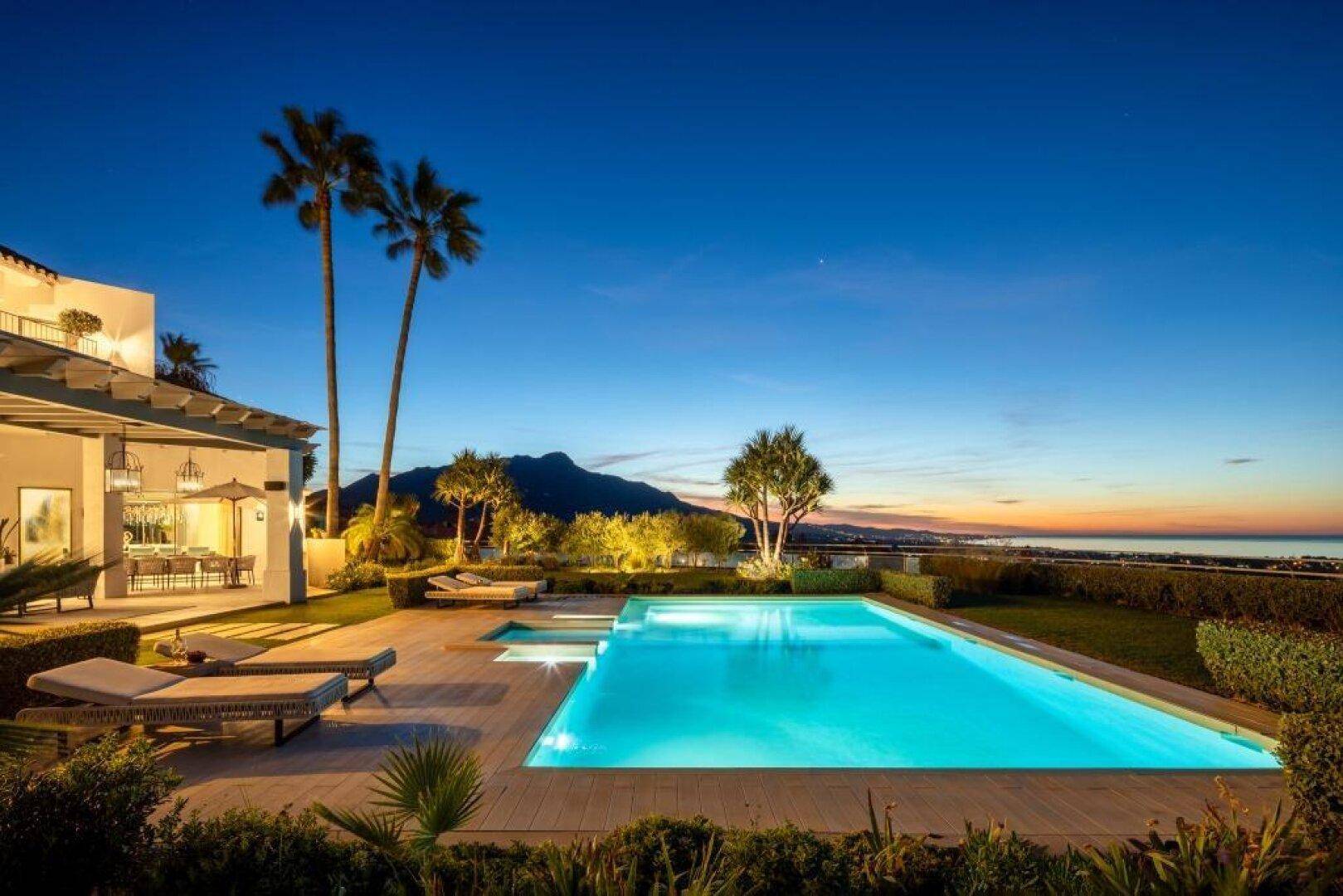 Abendansicht der beleuchteten Villa mit Pool, Bergen und Stadtlichtern in der Ferne.